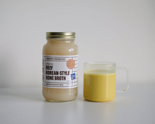 A jar of Reclamation Foods Korean-style bone broth beside a cup of golden milk made with broth